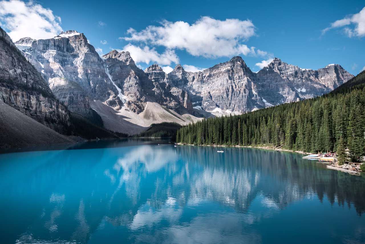 Aguas turquesas de un lago, rodeado de imponentes montañas nevadas y bosques de coníferas.